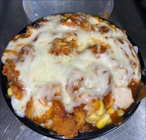 A bowl of fried chicken, corn and sauce topped with melted cheese