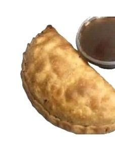 A baked pasty on a plate beside a small cup of homemade gravy