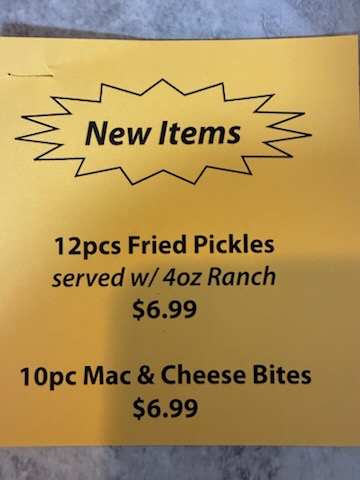 The yellow New Items sign from the deli counter listing fried pickles and mac and cheese bites